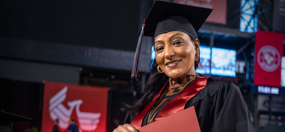 A graduate, wearing a black cap and gown, holds a degree in celebration at commencement.