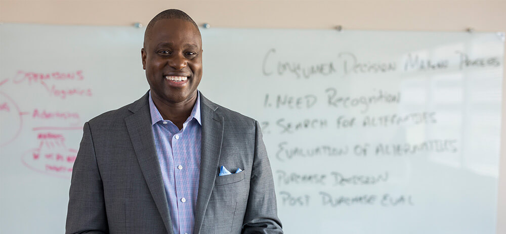 A professional man in a suit confidently stands in front of a whiteboard