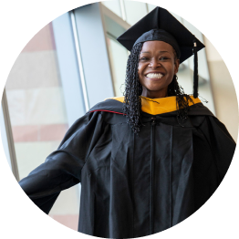A Phoenix alumni smiling while wearing their regalia