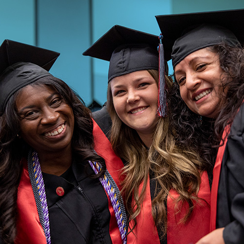 3 Graduates in their cap and gowns smiling at the camera