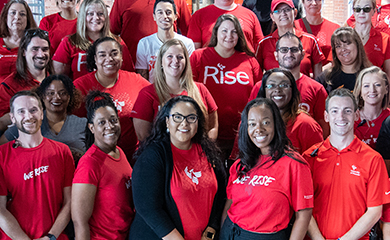 A group photo of alumni in University of Phoenix shirts smiling at camera