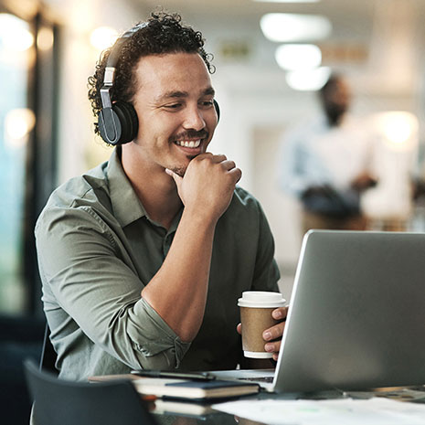 man smiling while working on laptop with coffee in hand