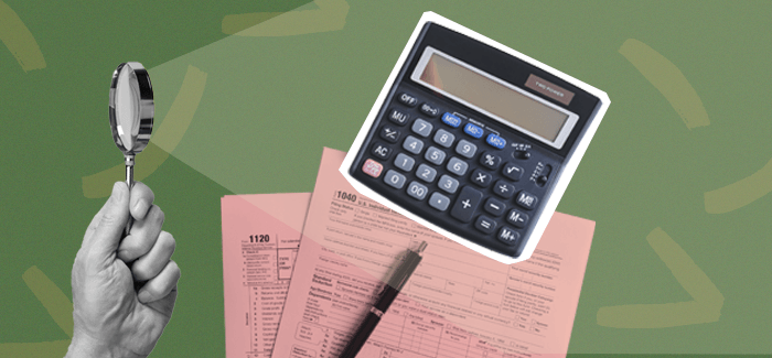 A hand holding a magnify glass shining a light over a calculator and tax documents to signify a tax examiner