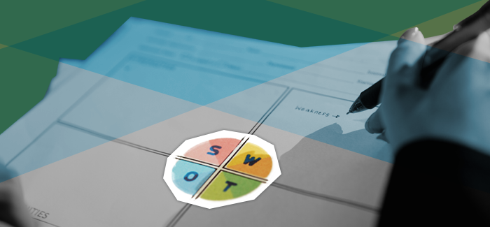 A hand holding a pen above a piece of paper used to map out a SWOT analysis that has SWOT written in a big circle in the middle