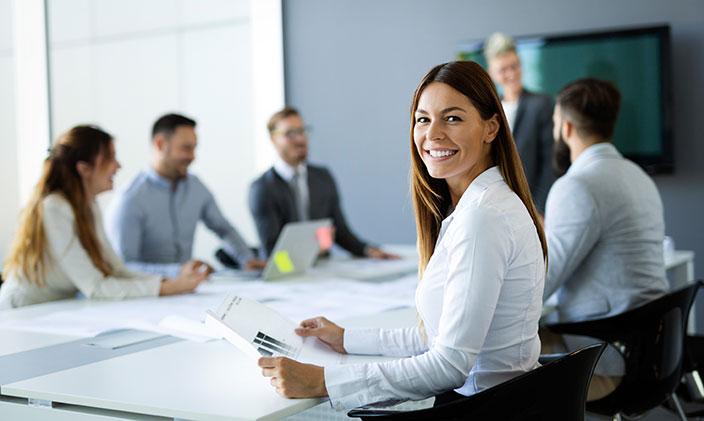 Smiling businesswoman working with coworkers sitting around a conference table discussing capital allocation.