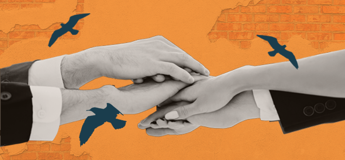 Four hands stacked on top of each other against a brick background with birds flying by to represent community corrections programs.