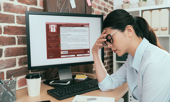 Frustrated woman working at desk, hand to forehead because she has to deal with ransomware attacks