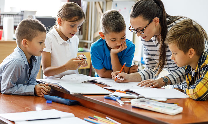 Female teacher looking over class assignment with young students