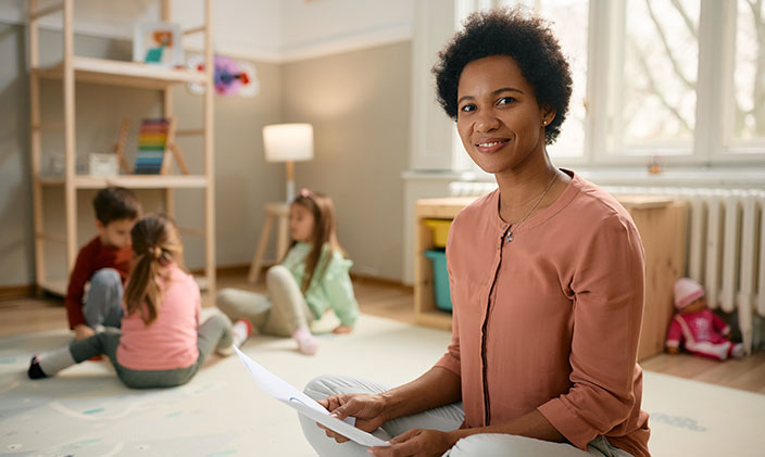 Kindergarten teacher sitting on the floor near three children to represent careers in elementary schools