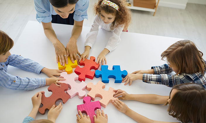A female teacher sitting in circle playing with oversize jigsaw puzzle pieces as a way to use experiential learning style.