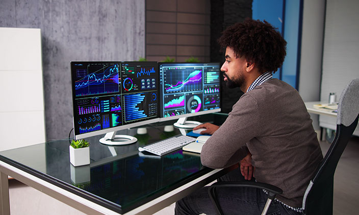 Financial analyst pores over data in a modern home office with two computer monitors