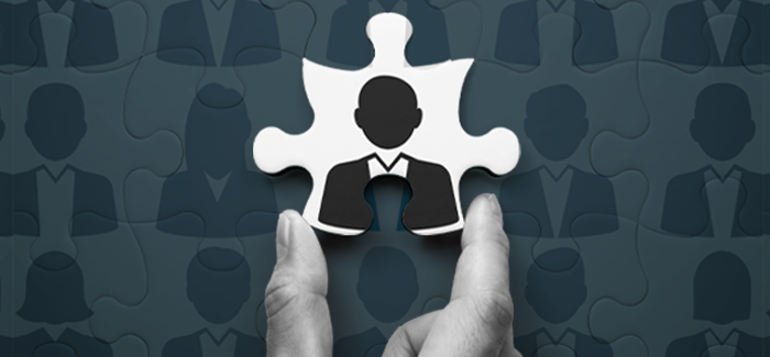 A hand holding a puzzle piece with a silhouette of a man on it, in front of a puzzle to signify the role of an HR manager