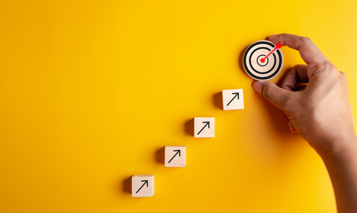 Four wooden blocks with arrows on them pointing to a round wooden target to signify performance management