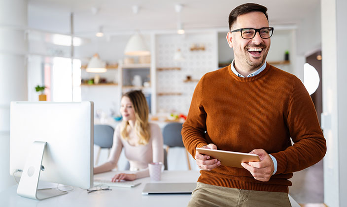 Male IT support specialist holding a tablet and smiling, women working in the background