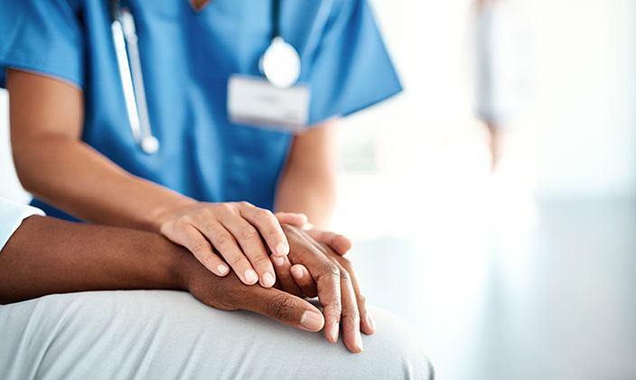 Cropped photo of a nurse holding onto a patient's hand to signify the nursing model vs medical model of patient care