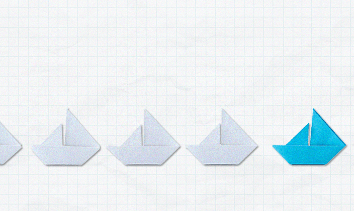 Paper sail boats in a row, the leading one is blue while the others are white to signify nursing leadership