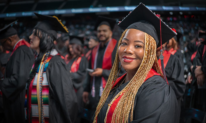 Graduate standing at a ceremony in cap and gown smiling at the question "is a master's degree worth it?"