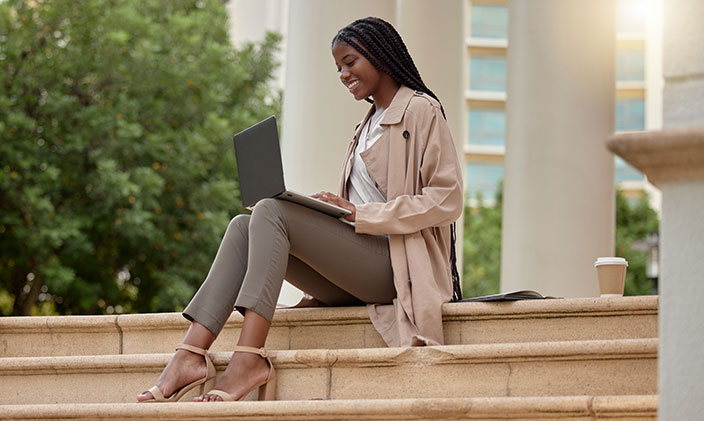Professional using laptop while sitting on building steps admiring her digital badges