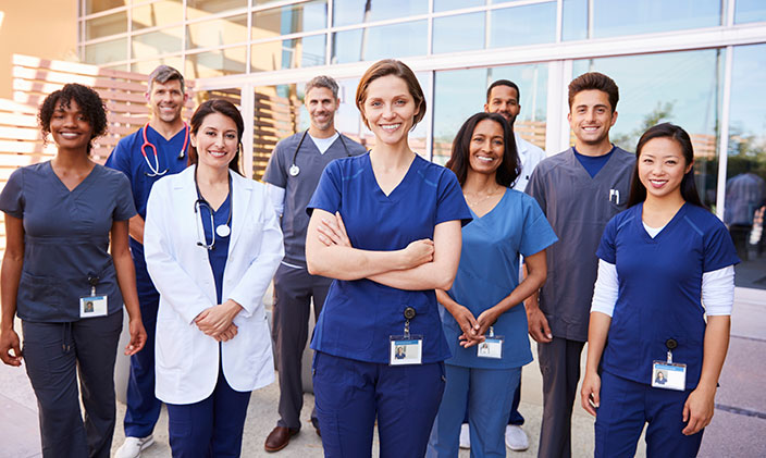 Group of healthcare professionals smiling and standing in front of hospital