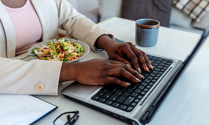 Woman typing on laptop and eating a salad