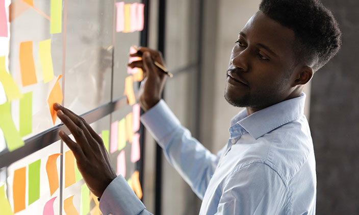 Young Black businessman checks his Post-Its on a whiteboard