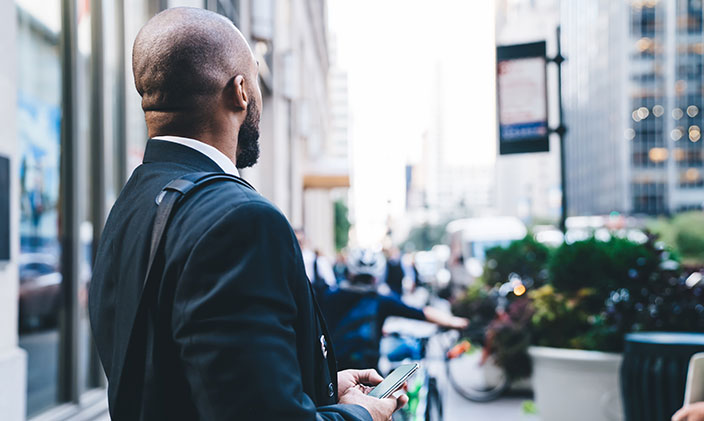Businessman stands on a sidewalk, facing traffic, in a major metropolitan city