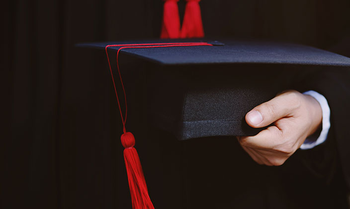 Male graduate holding a graduation cap.
