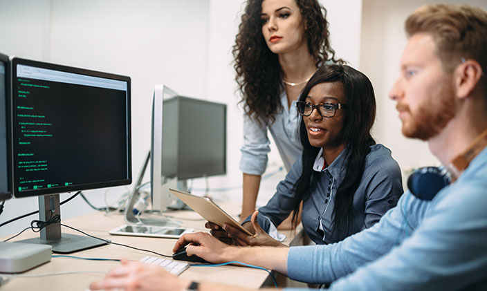 Three business professionals, two women and one man, working on a computer information systems project