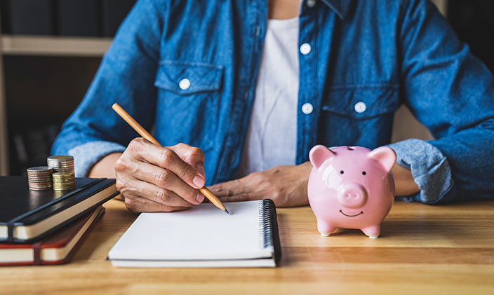 woman writing in notebook with coins and piggy bank next to her