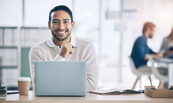 Young male entrepreneur smiling and working in a coffee shop to signify disruptive innovation 