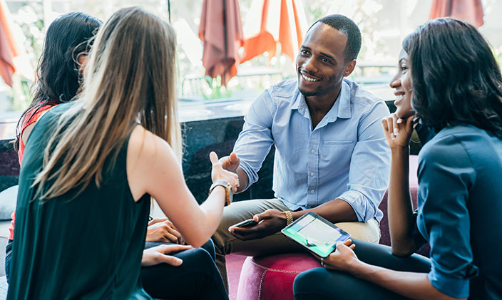 Three women and one man sitting in a circle, man and woman shaking hands, to represent an alumni association