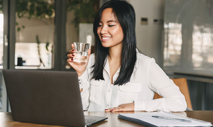 Smiling Asian woman, drinking water while using laptop