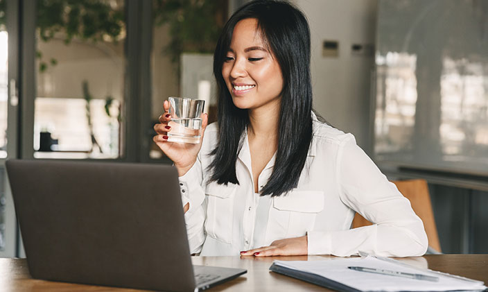 Smiling woman, drinking water while using laptop