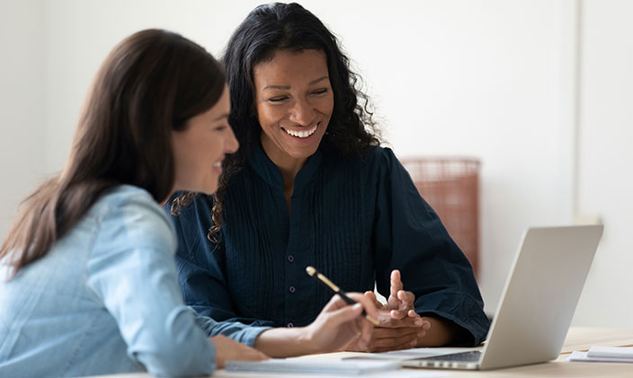 Two female co-workers overlooking laptop work together