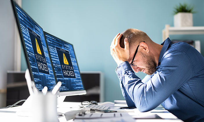 Man looking upset with his hands on his head, looking at computer that has been compromised by a virus