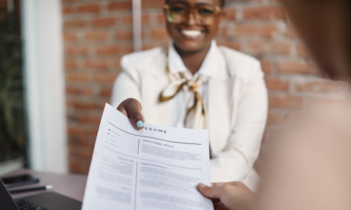 Sharp dressed black woman handing over her resume or curriculum vitae to a prospective employer.
