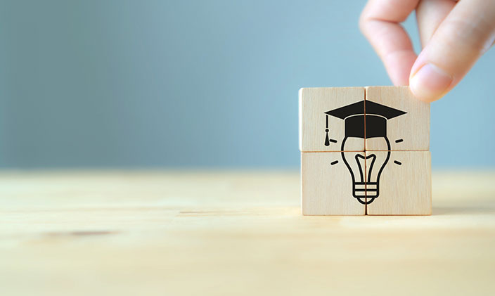 Fingers holding up a tile with a lightbulb and graduation cap