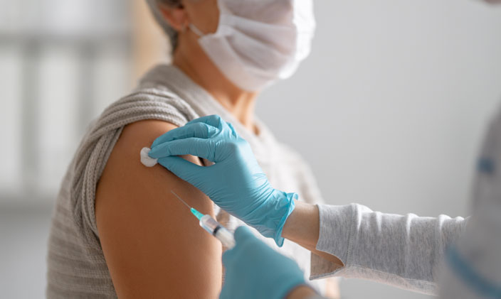 Person with a mask on receiving a shot from a gloved nurse