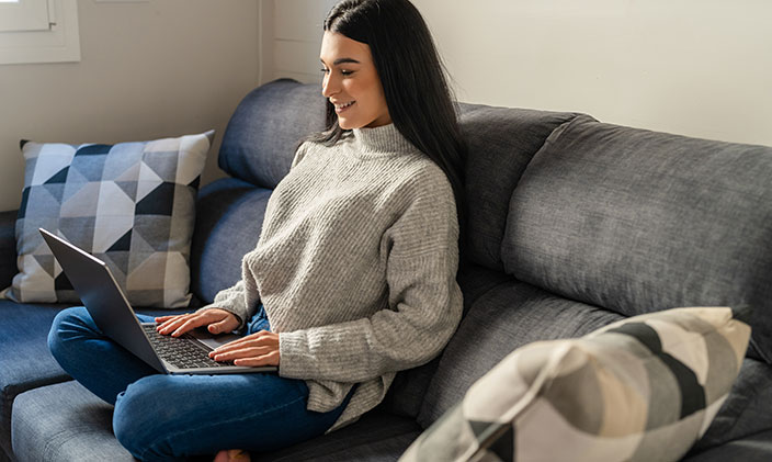 Young woman smiles while taking an online course from her couch