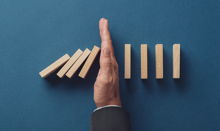 Hand stopping falling dominos to signify risk management