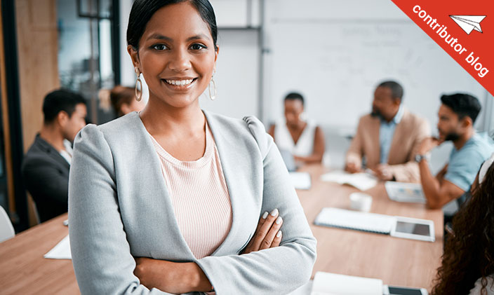 Business woman smiling with people at a meeting table in the background