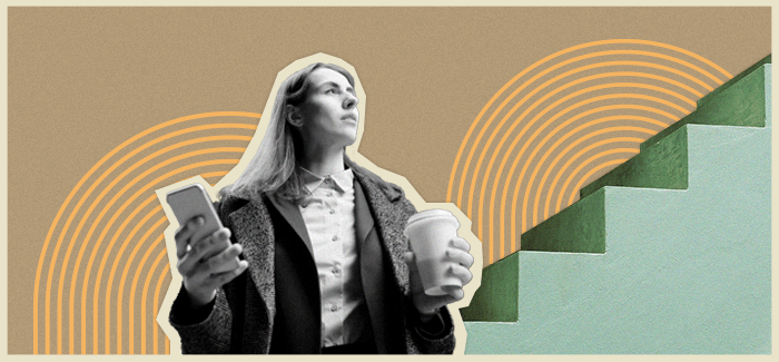 Businesswoman with phone and coffee looking up next to stairs.