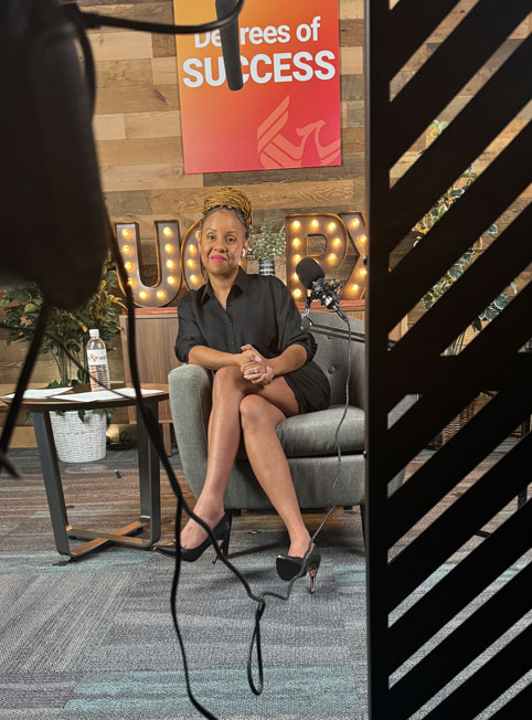 Freda Richards in a black outfit, seated in the podcast studio with camera and microphone equipment partially visible in the foreground.