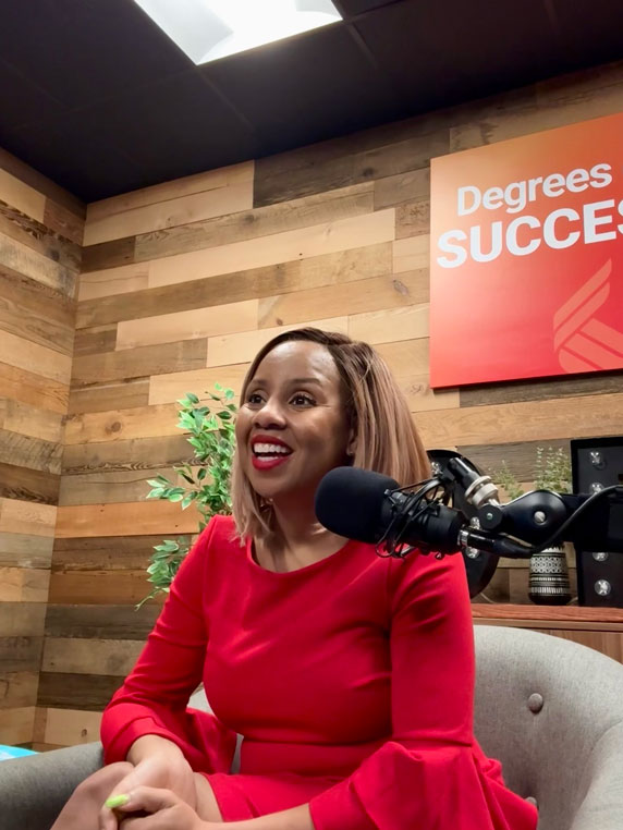 Freda Richards sitting in front of a microphone in the Degrees of Success studio, smiling in a red dress with a wood-panel background and podcast signage.