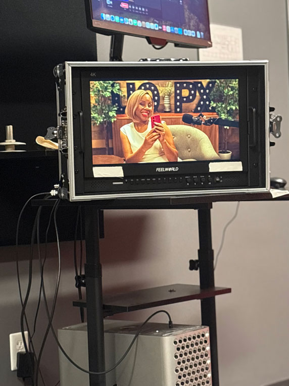 A monitor showing Freda Richards smiling and holding her phone during a recording session in the Degrees of Success podcast studio.