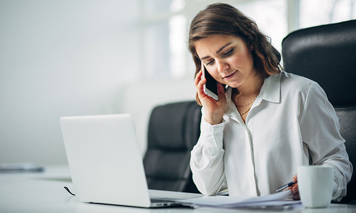A case manager uses a mobile phone and laptop while looking over some case files