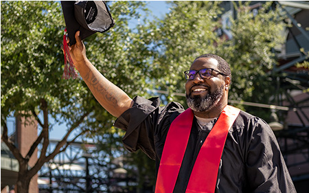 University of Phoenix graduate celebrates by raising their cap in the air