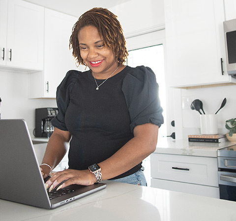 A woman in her kitchen, working on her laptop