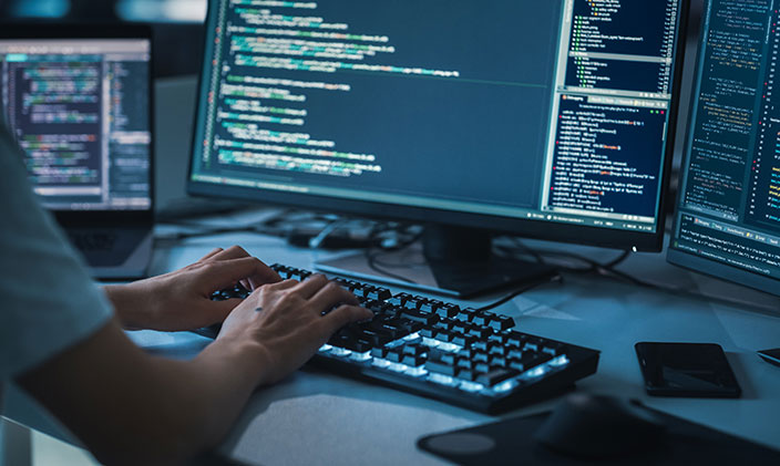 Hands on keyboard centered among three computer monitors