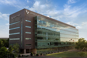 Link to an image of th University of Phoenix building, centered in the image, with a blue sky and light clouds behind it